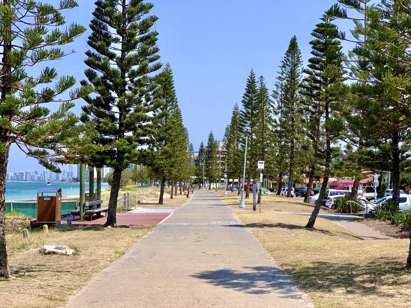 walking-from-bayview-beach-foreshore-path The paved Broadwater foreshore path at Biggera Waters on the Gold Coast, lined with Norfolk Island pines, with the Broadwater alongside