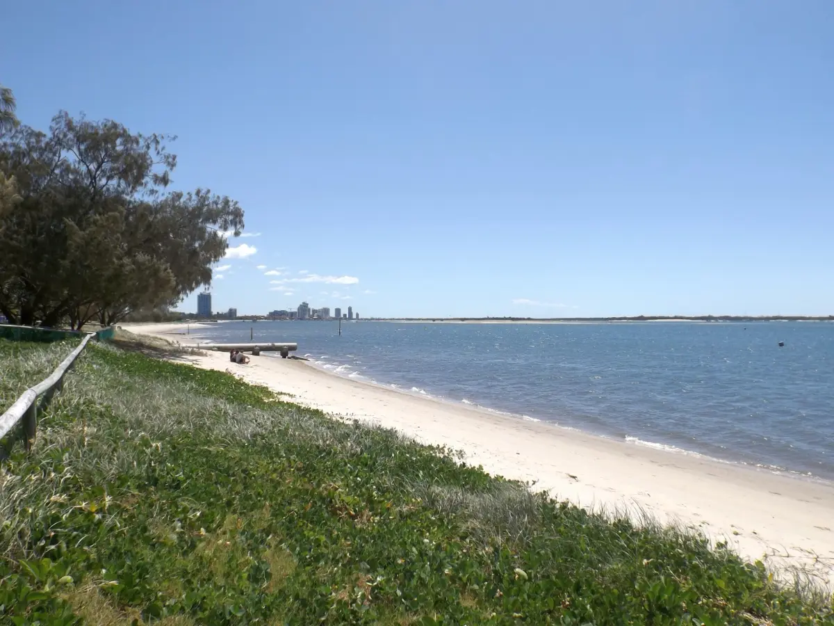 Sandy foreshore and grassy dune at Broadwater Parklands, Southport, with the Southport skyline across the Broadwater